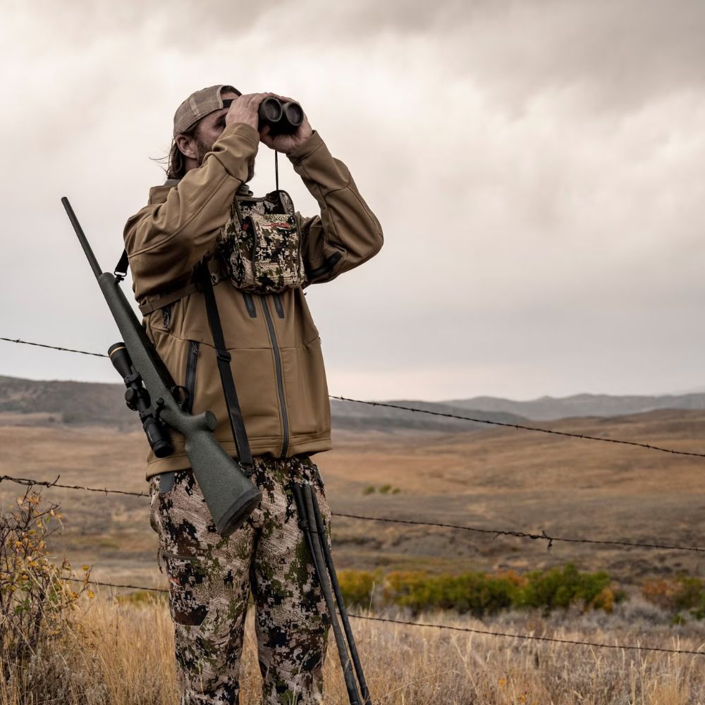 Hunter in camouflage gear using binoculars in a desert landscape